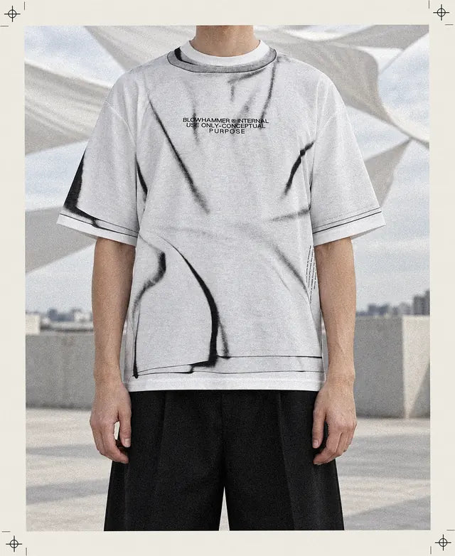 Une personne inventée, coupée au cou, porte le tee-shirt Crux blanc aux plis imprimés avec l'inscription noire sur la poitrine, sur une terrasse avec de grandes voiles blanches tordues par le vent.