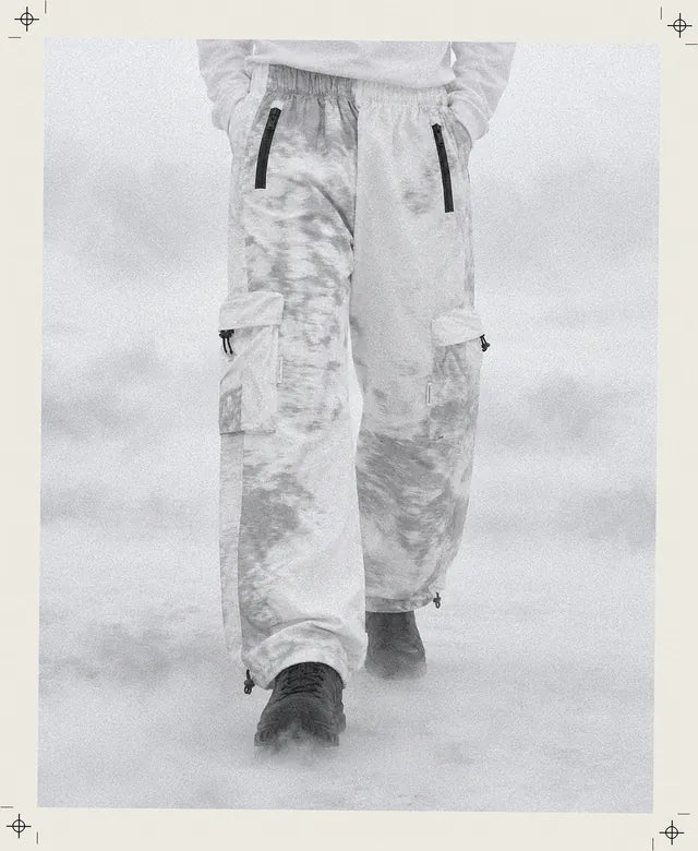 Una persona inventada, encuadrada de cintura para abajo, camina en la niebla por una llanura blanca con el pantalón cargo Grey Noise blanco de nubes grises, y solo se ven las cremalleras negras.