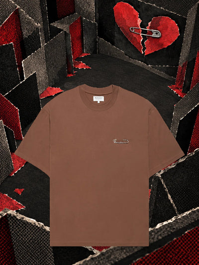 The brown Brokenheart t-shirt in a room of dark paper, under a red paper heart broken in two.