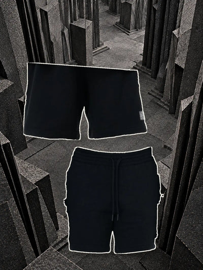 The black Classic Black bermuda shorts seen from the back, hanging on a thread, and from the front with the drawstring, among blocks of dark paper.