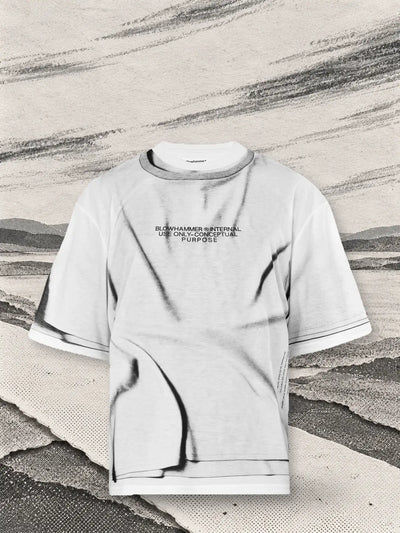 The white Crux t-shirt above a crossing of white paper paths, with long streaks of grey charcoal carried by the wind.