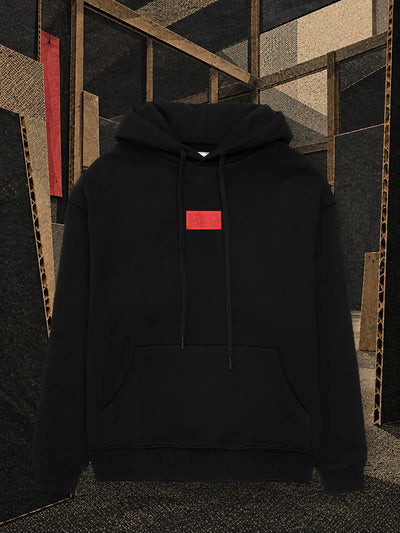 The black Deconstructed hoodie in a half finished cardboard workshop, with a red strip hanging from a beam.