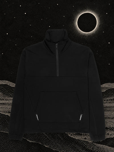 The black Eclipse half zip sweatshirt on black paper dunes, under an eclipse with a ring of white light.