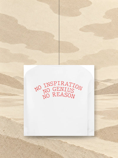 A piece of the back print of the white No Inspiration hoodie, with the red lettering NO INSPIRATION NO GENIUS NO REASON, hanging on a thread above a field of ivory paper.