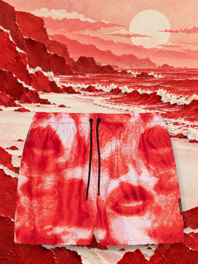 The red and white Noir swim shorts on the shore of a sea of red and white paper waves, under a pale sun.