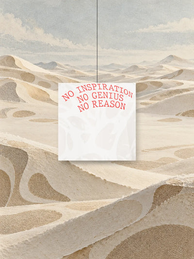 Un quadrato ritagliato dalla stampa della felpa Strand Ivory, con la scritta rossa NO INSPIRATION NO GENIUS NO REASON, appeso a un filo sopra dune di carta avorio.