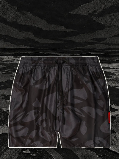 The black Strand swim shorts, with a pale paper border, on the shore of a black paper sea.