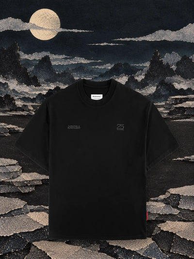The black Vertebrae t-shirt on a black paper plain at night, among rows of stacked grey paper stones and the moon.
