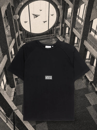 A t-shirt preta Travel Agency numa sala de espera de papel, com aviões de papel pendurados diante de uma grande vigia.