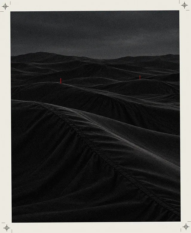 Um deserto de dunas pretas que parecem tecido técnico, com pregas e costuras, e ao longe duas pequenas estacas vermelhas.