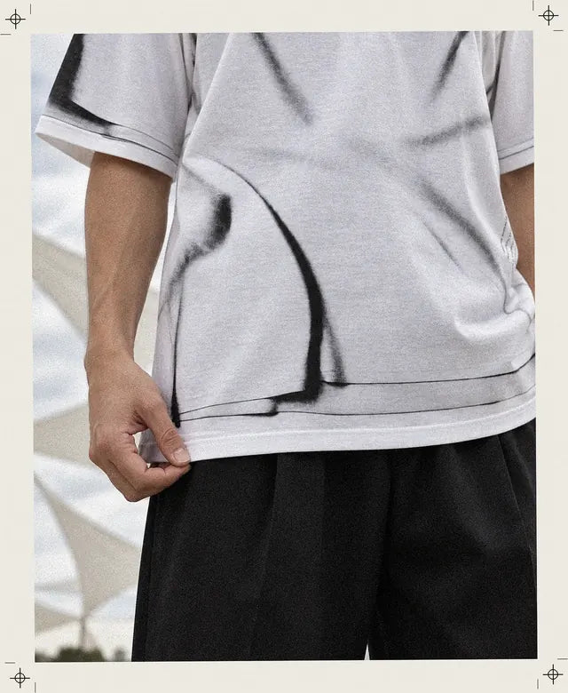 Les doigts tiennent l'ourlet blanc du tee-shirt Crux, juste sous le second ourlet qui n'est qu'imprimé, avec un long pli noir dessiné qui descend jusqu'au bord.